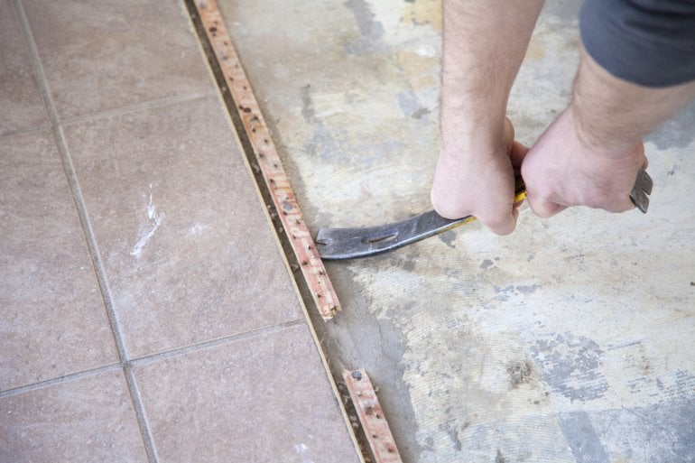 A man uses a pry bar to remove tack strip from a floor.